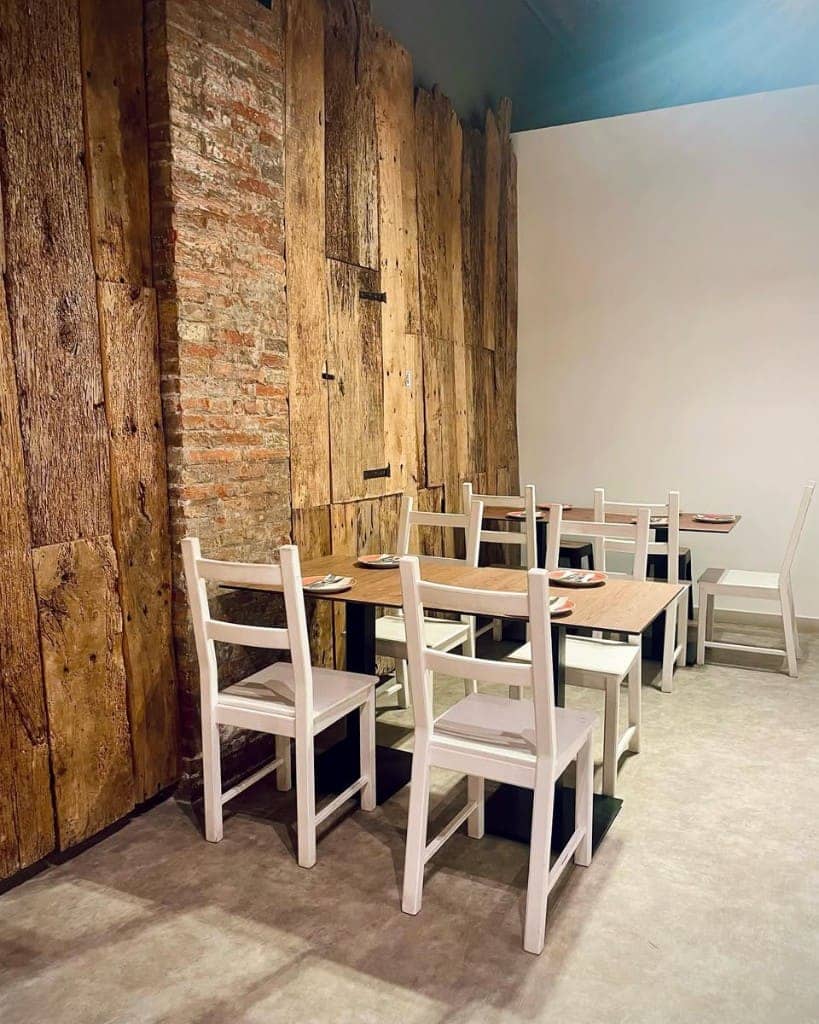Interior de BarK amb parets de fusta i totxo, taules de fusta i cadires blanques